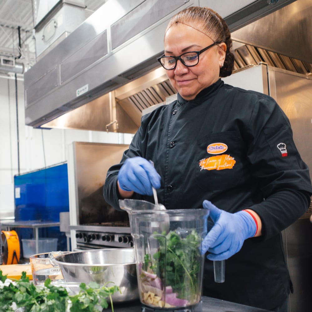 A woman puts vegetables in a blender at YVR Prep