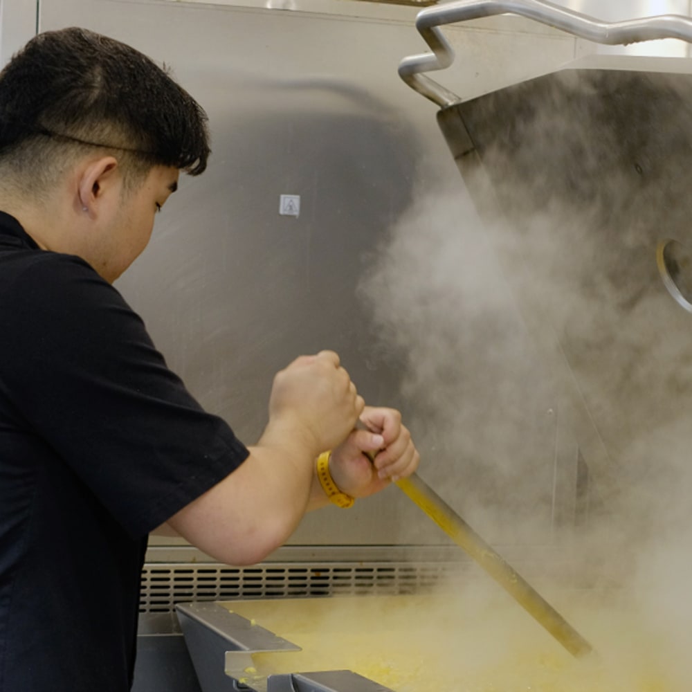 A man stirs a big vat of hot liquid at YVR Prep